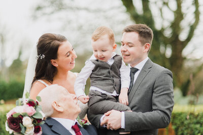 A couple on their wedding day holding their child with their father looking at them taken by Devon Wedding Photographer Liberty Pearl