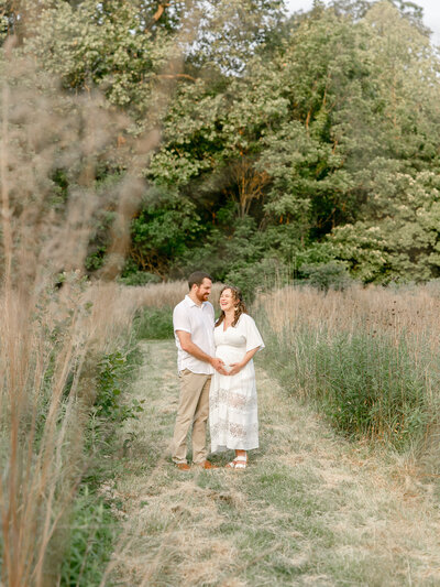 A couple walking in a field with hands on the pregnant belly of the woman