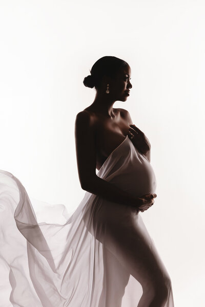 black pregnant mom posing in white dress for maternity portraits in phoenix maternity studio
