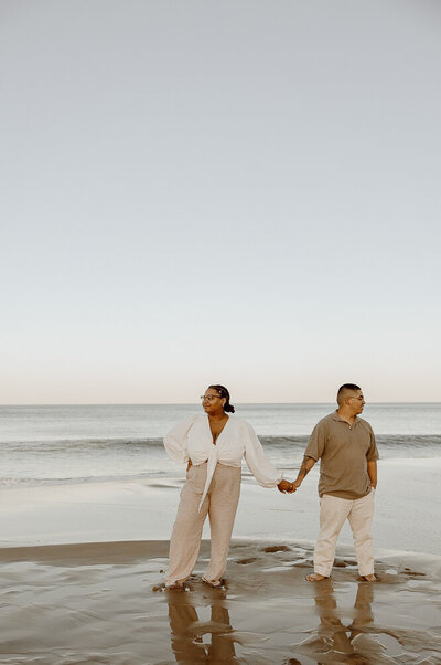 Couple stands at the edge of the beach facing opposite directions