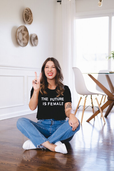 Emylee Williams sits cross-legged on the floor in her signature “Future is Female” shirt, symbolizing her bold stance against cookie-cutter business models. The image reinforces her authority-driven, no-BS approach to business growth.