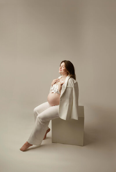 Studio maternity portrait of a pregnant woman dressed in neutral tones, softly lit against beige background, evoking elegance and grace in Minneapolis Minnesota