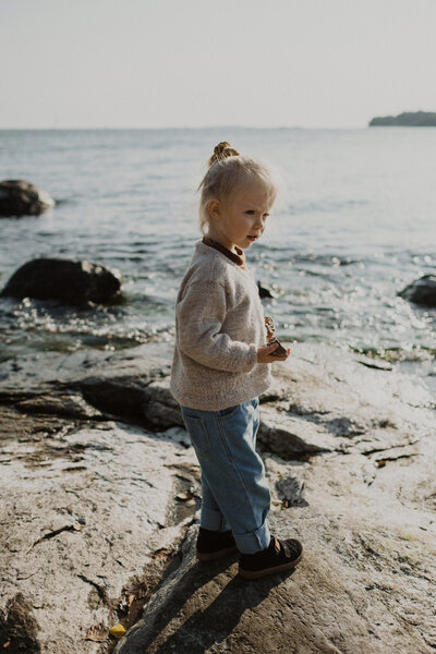 3-vuotias tyttö seisoo rantakalliolla ja pitelee kiviä kädessään Lauttasaaressa Helsingissä