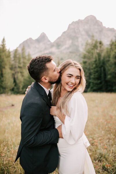 bride laughing while groom kisses her cheek after their teton elopement taken by adrian wayment.