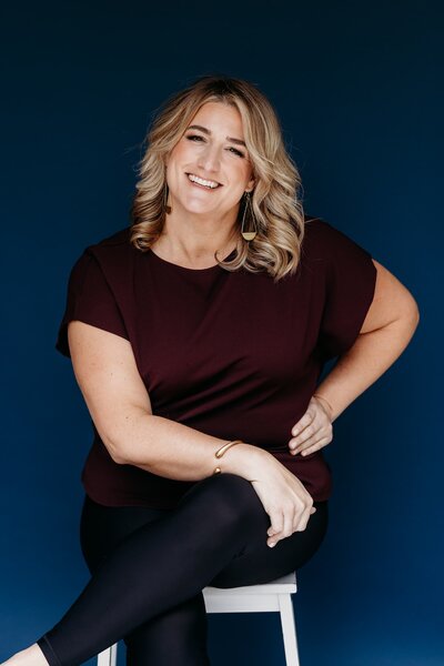 Austin maternity and newborn photographer Jen Rizy, owner of Hello Photography, sitting in studio with camera and smiling.