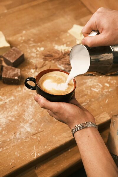 hands pouring steamed milk into a cup of espresso