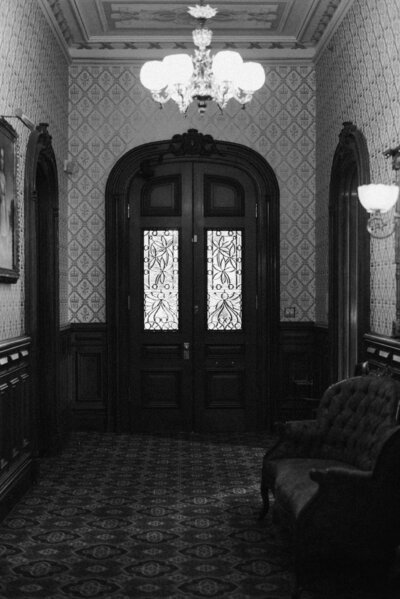 Black and white film-style wedding photograph capturing the interior front door of Common House in Richmond, VA, setting the scene for an elegant wedding day.