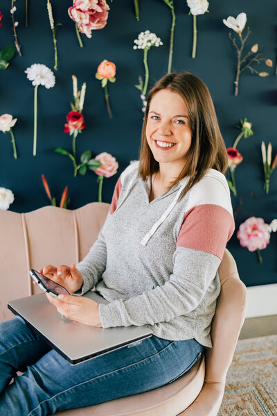 casual headshots of denver photographer smiling at the camera while sitting on a light pink couch against a blue wall