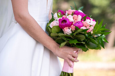 A bride in a white dress holds a vibrant bouquet of pink and white flowers, smiling joyfully on her wedding day