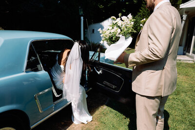 Groom helping his bride into vintage car on their wedding day
