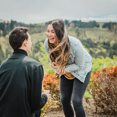 A person smiling as their partner is on one knee proposing in front of them 