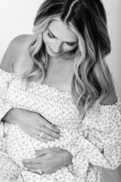 Close-up of a pregnant belly with the mother gently resting her hands on it, wearing a vibrant blue floral dress