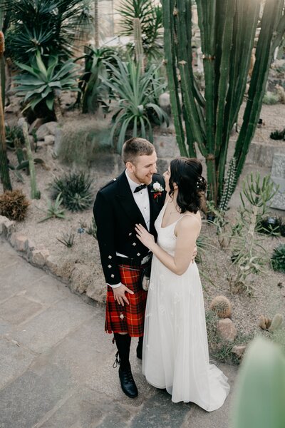 A wide overheard view of a wedding couple as they wrap their arms around each other in David Welch Winter Gardens in Aberdeen. They are surrounded by cacti in a botanical glasshouse.