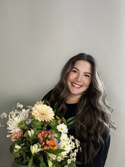 Ashley smiles at the camera while holding a bouquet of flowers. Representing her vendor profile for the Crush Collective wedding show.