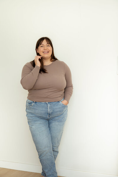 Chantal Hewitt smiling and standing in front of a white wall wearing a brown shirt and blue jeans - Family Autism Support Coach at Chantal Hewitt Coaching4