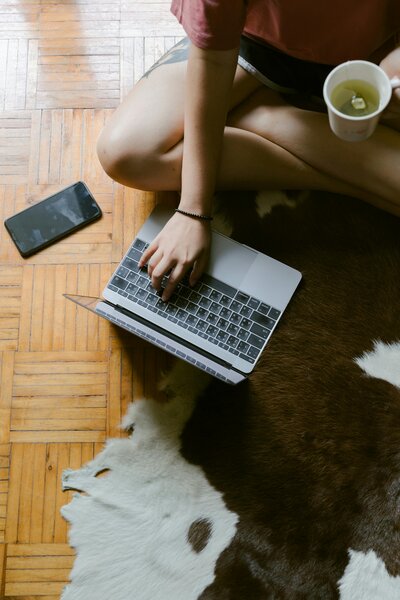 A person sitting on the floor with a laptop and phone nearby, working in a cozy setting.