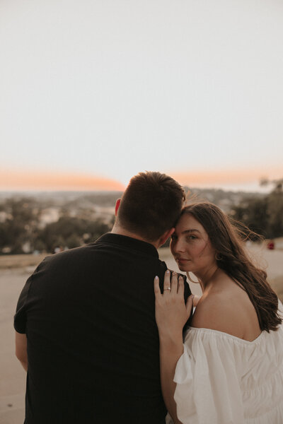 golden hour sunset engagement photos with white dress on bride and black shirt on groom. wedding ring inspiration and windy hair