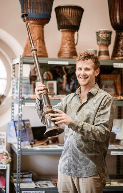 Daniel Scruggs smiling with a long horn in front of his instrument collection