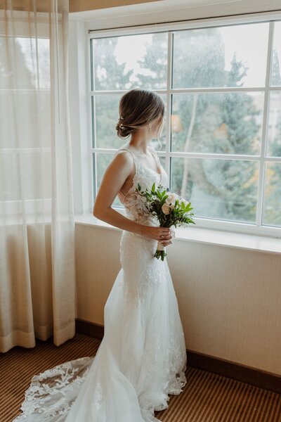 Bride with small green bouquet looking out the window