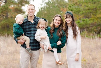 Family of five wearing a combination of forest green, cream and dark blue colors in a field in Lexington SC