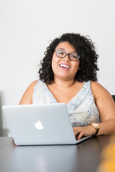 Smiling woman using a laptop to file her taxes, representing a basic individual 1040 tax return service starting at $99 including one state return