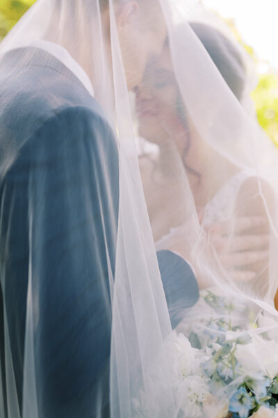 Romantic portrait of a bride and groom underneath a wedding veil with muted soft colors and diffused light