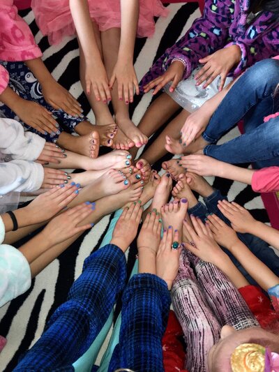 Girls sitting in a circle showing their colourful manicure and pedicures done by the Feel Fabulous nail technicians.
