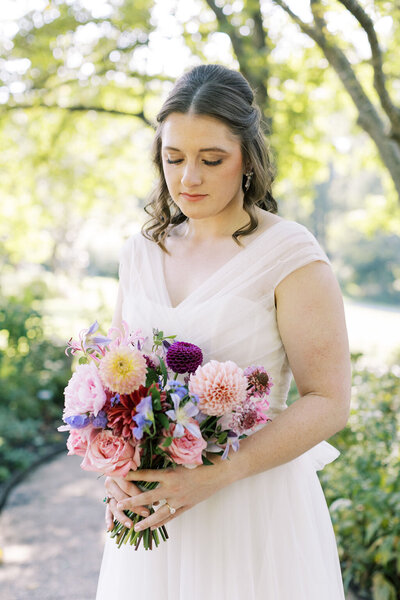 A summer bride wearing a white tulle looks down as she holds a bouquet of flowers surrounded by nature at Meadowlark Botanical Gardens