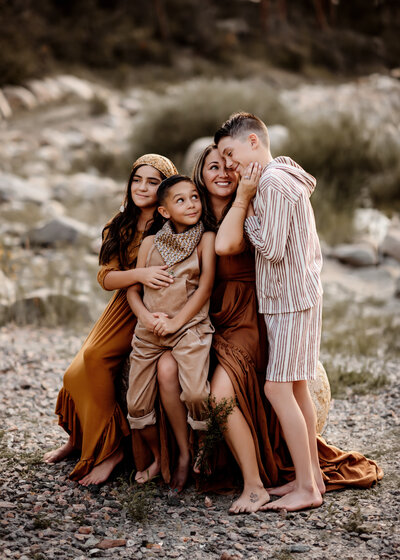 A mother wearing a red dress holding her oldest son while her youngest hugs her back in Wyoming field
