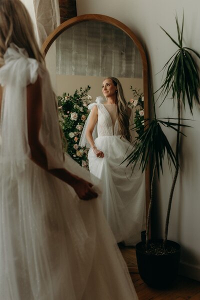 A lovely bride spins in her whimsical wedding dress in front of a mirror.