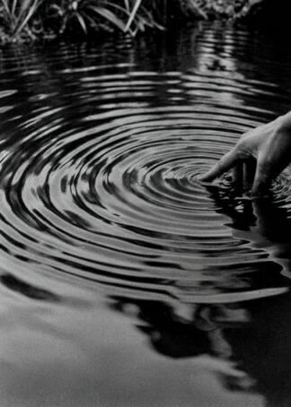 A hand gently creating ripples in still water, symbolizing transformation and the ripple effect of small actions.