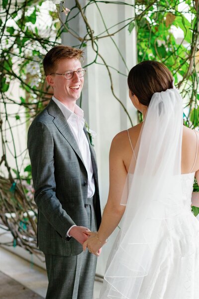 A newlywed couple holding hands and smiling at each other 