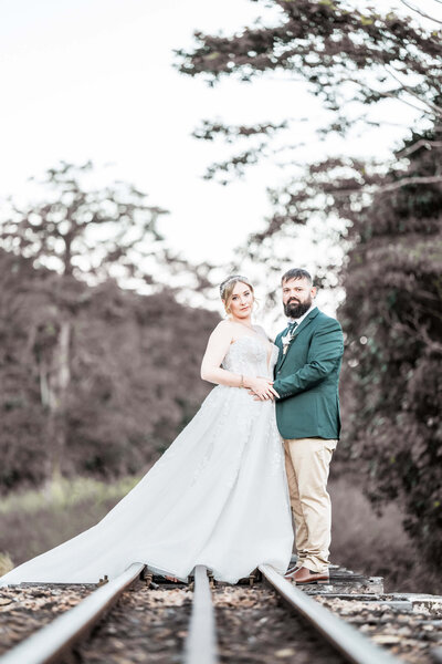 A bride and groom stand together on train tracks surrounded by lush woods, symbolizing love and adventure. - photo by Jamie Simmons