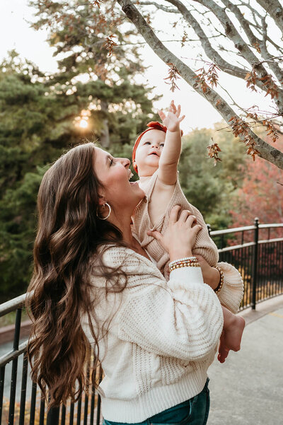 Mama holding her baby reaching for leaves during a family photography session in Charlotte by Tonya Cassibry, capturing tender, candid moments.