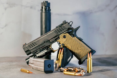 Staccato 2011-style handgun with tan textured grips, surrounded by ammunition, magazine, and suppressor, captured by Joseph Mayden for tactical branding and product marketing.