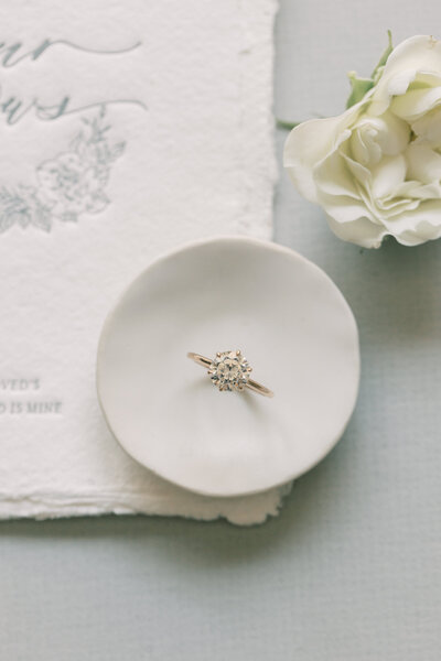 Engagement ring perched on a small round jewelry dish on top.