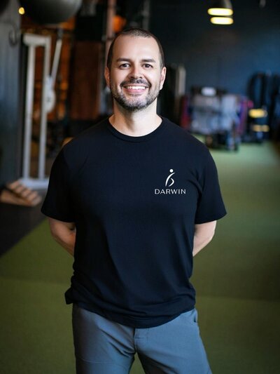 Darwin Ruiz wearing a black T-shirt with a smaller logo placed over the left chest, showcasing a more understated brand presence in an athletic environment.