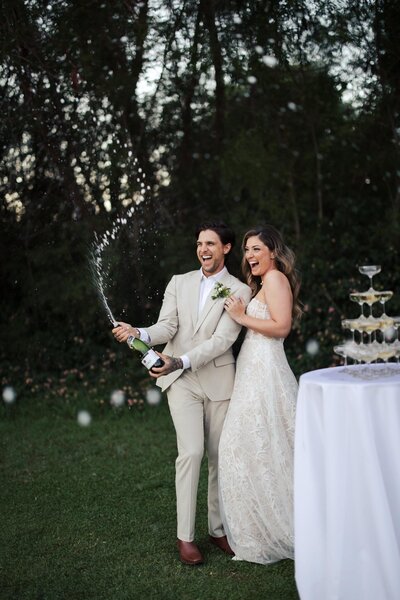 Bride and groom popping champagne next to a table