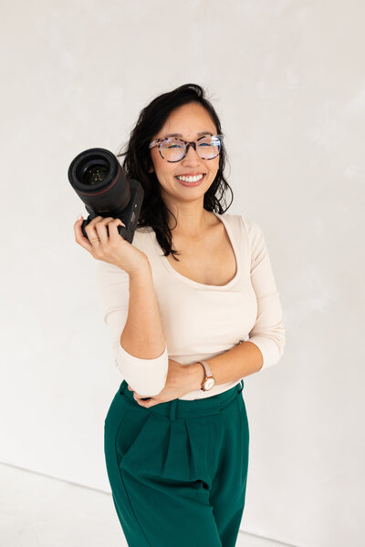 Anh Nguyen, UNC & Duke graduation photographer, smiling at the camera during a studio portrait session while holding camera.