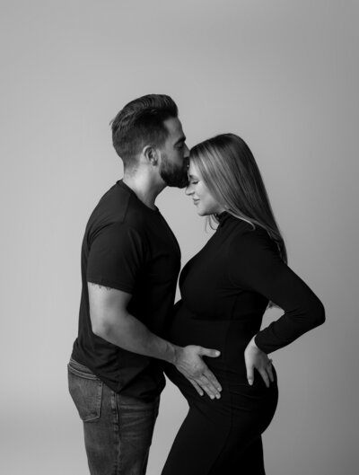 husband kissing wife's forehead while holding her belly