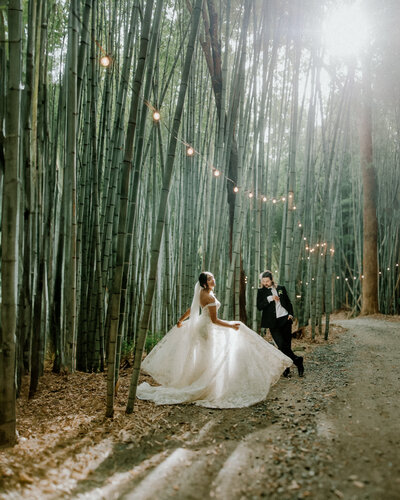 Bride dances in the sunlight in a bamboo forrest while groom watches
