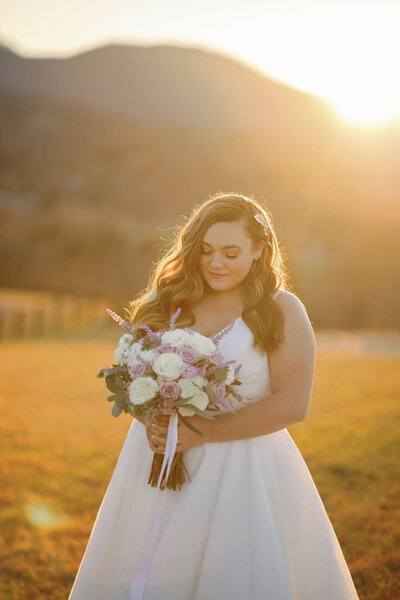 bride at sunset holding a floral bouquet and gently smiling at the flowers while the sun shines behind her for her Gatlinburg elopement