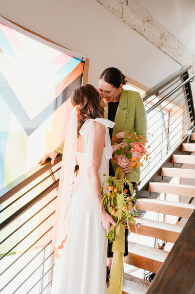 Brides kissing and holding their wedding flower bouquets on a staircase.