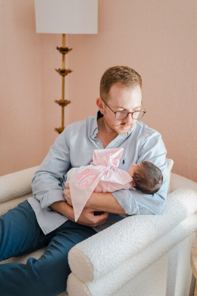 Mom cradles a sweet newborn and dad has his arms wrapped around both of them and smiles at his new daughter.