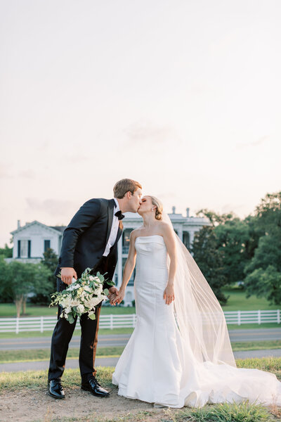 A couple kisses while standing before Nottoway Plantation at sunset.