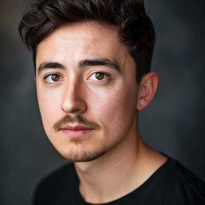 Professional headshot of young man in black shirt looking confidently forward against neutral studio background new york.
