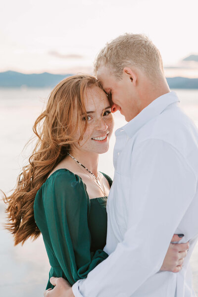 A man and woman stand smiling with mountains in the background