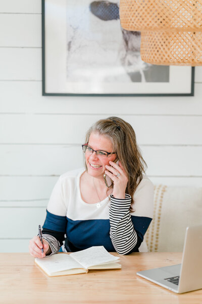 Lead brand photographer Amanda Richardson takes notes while talking on the phone with a client