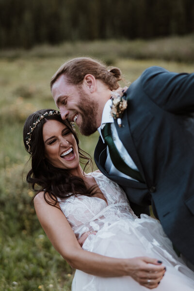 Bride and groom laugh joyfully in a wildflower meadow near Breckenridge, Colorado.