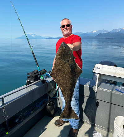 A man with short grey hair holding a halibut on a juneau boat rental power boat